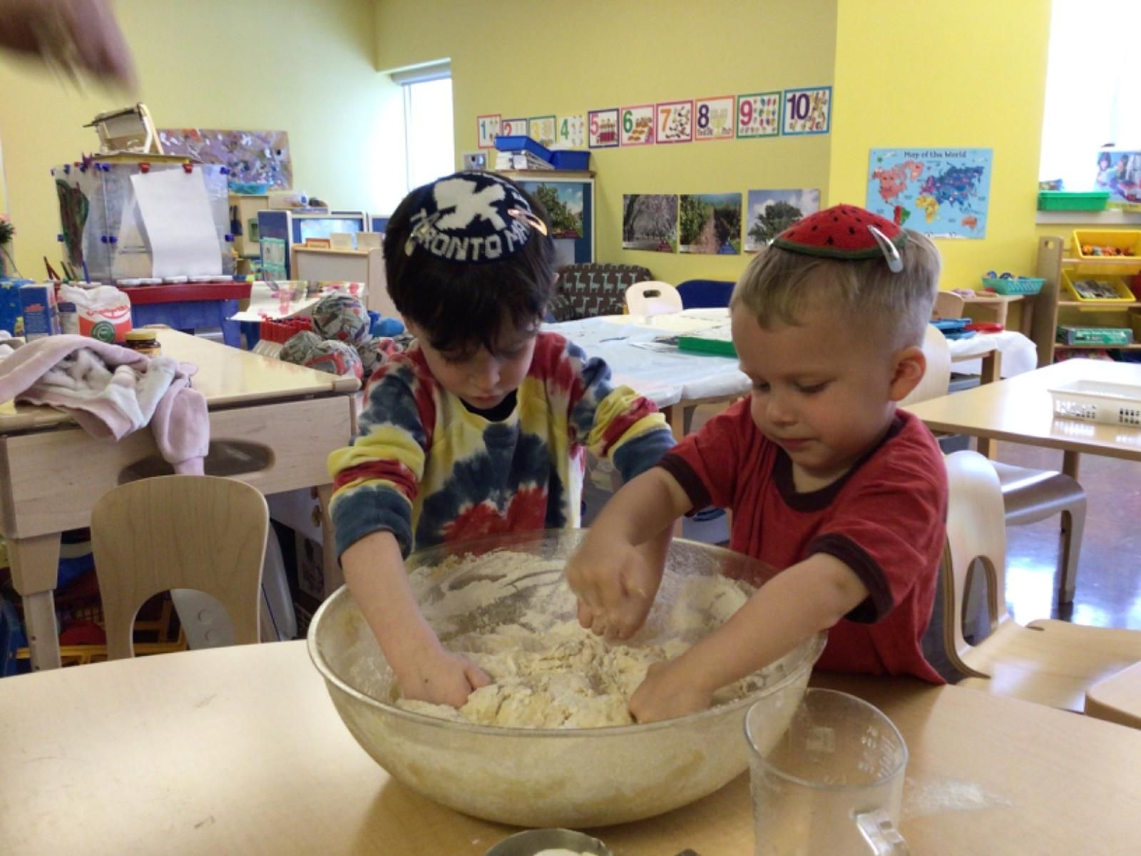 Two young boys are kneading dough in a bowl in a classroom