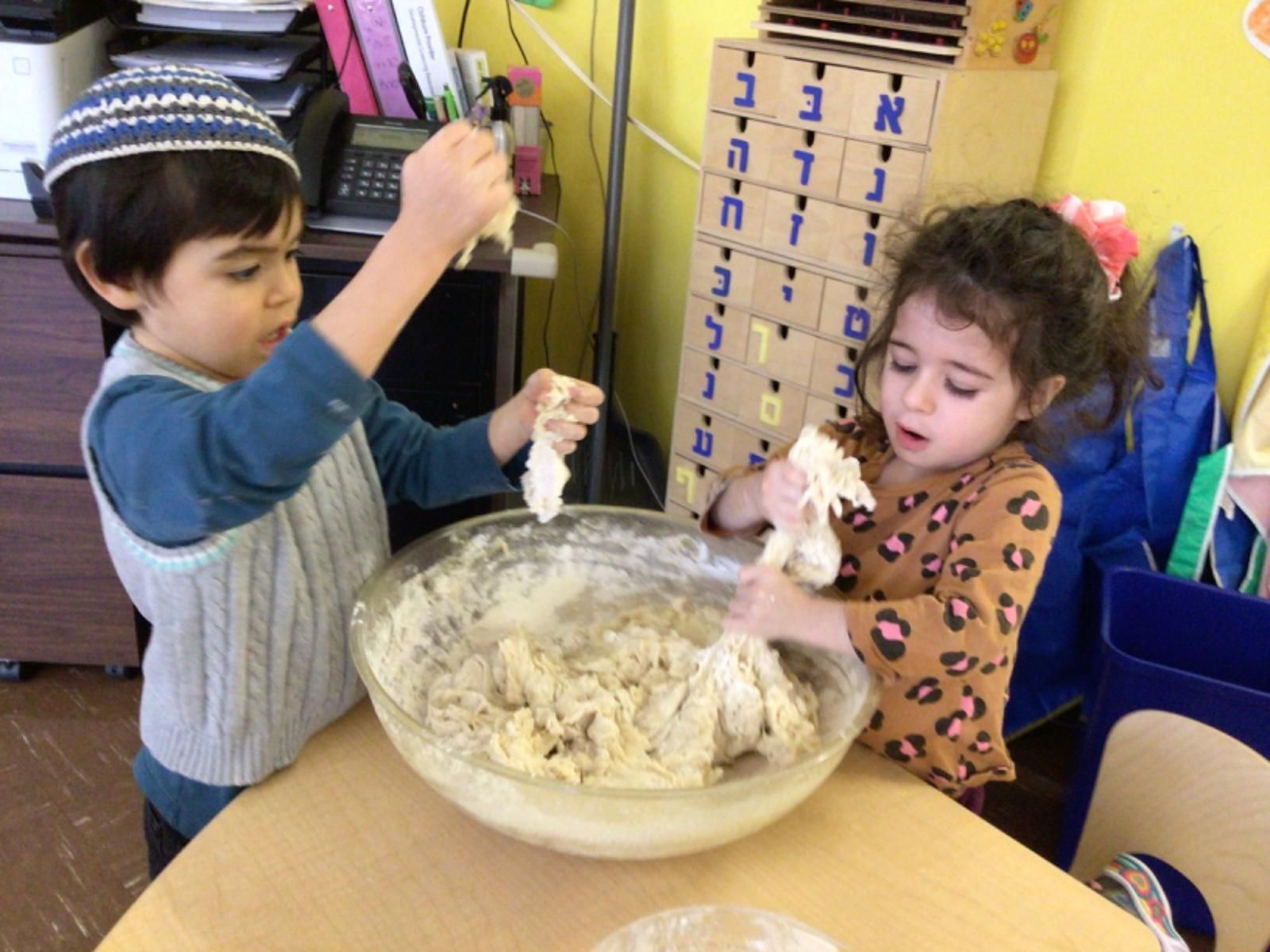 A boy and a girl are mixing dough in a bowl