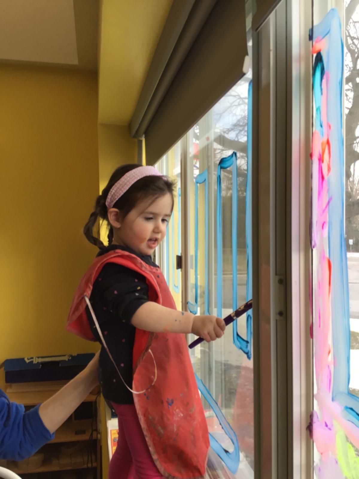 A little girl is painting a window with a brush