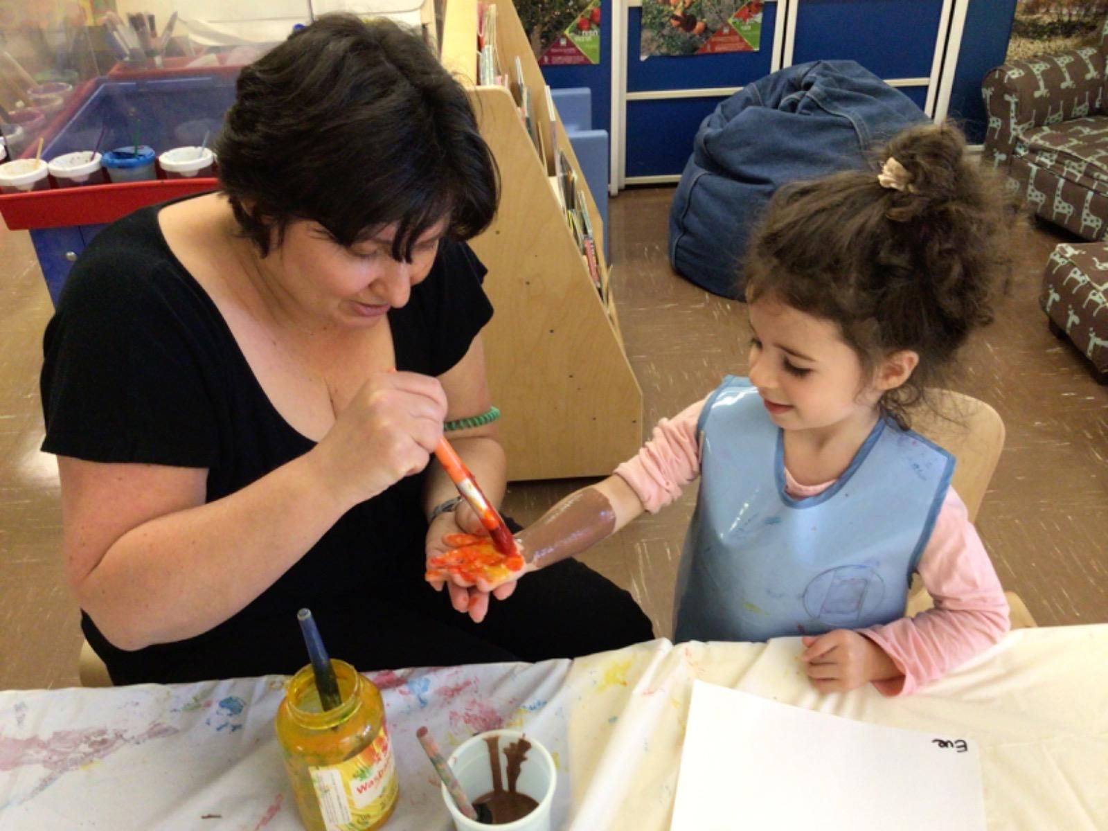 A woman is teaching a little girl how to paint