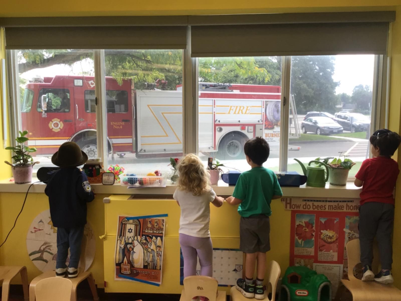 Three children are looking out a window at a fire truck