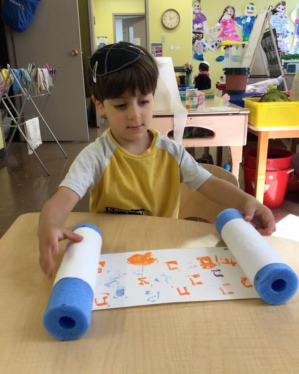 A young boy is sitting at a table holding a piece of paper with hebrew writing on it