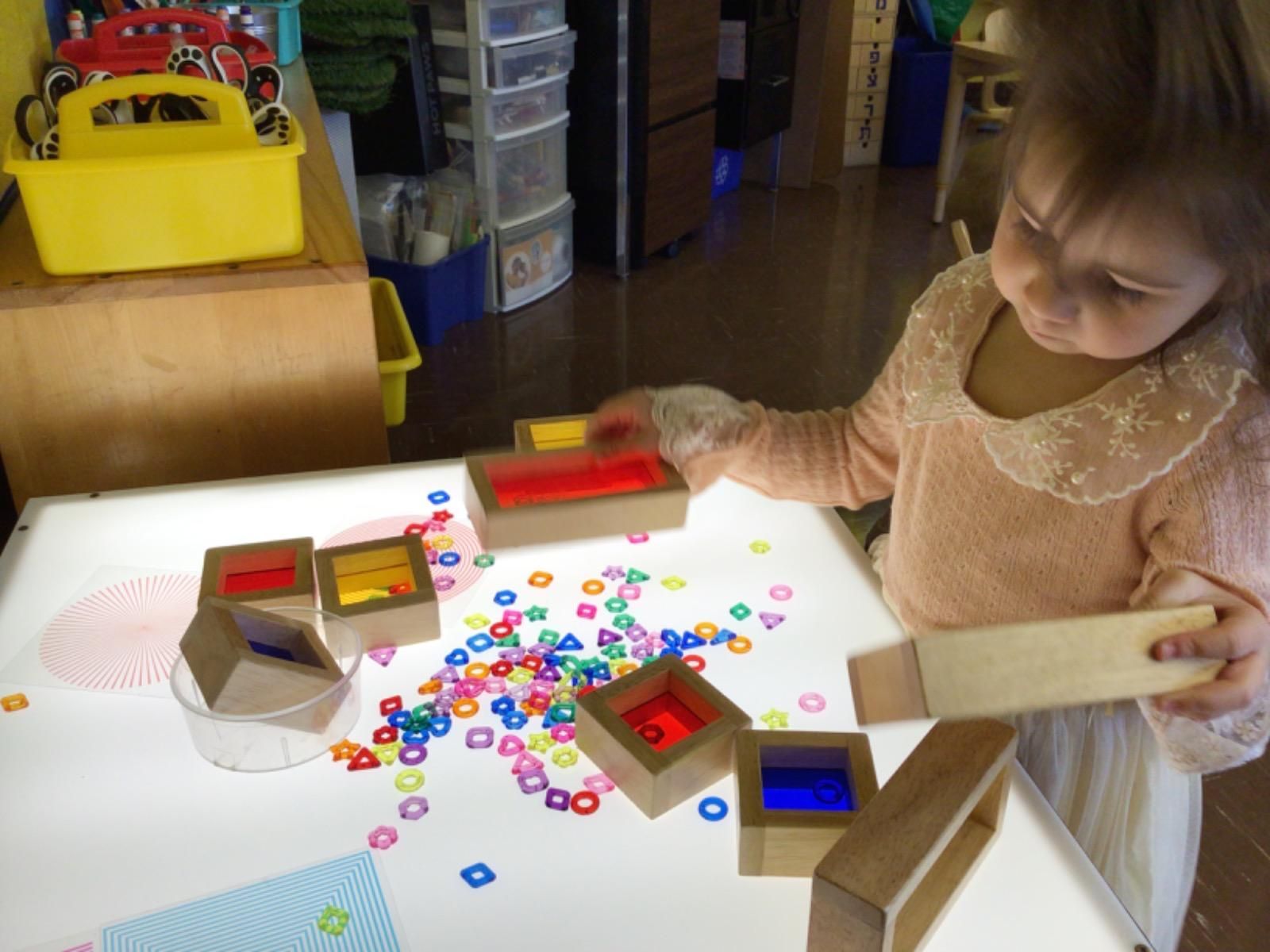 A little girl is playing with wooden blocks on a light table