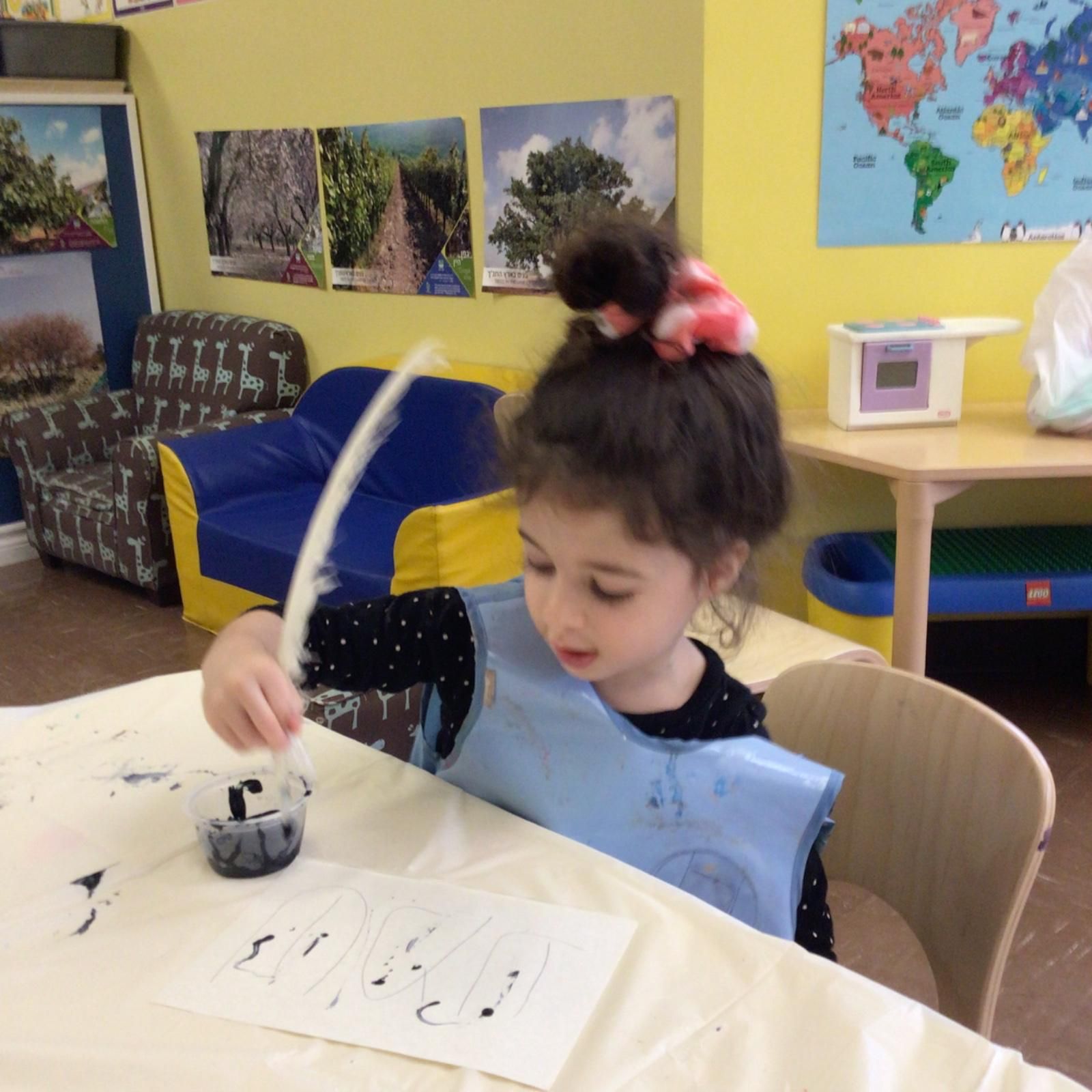 A little girl is sitting at a table writing with a feather