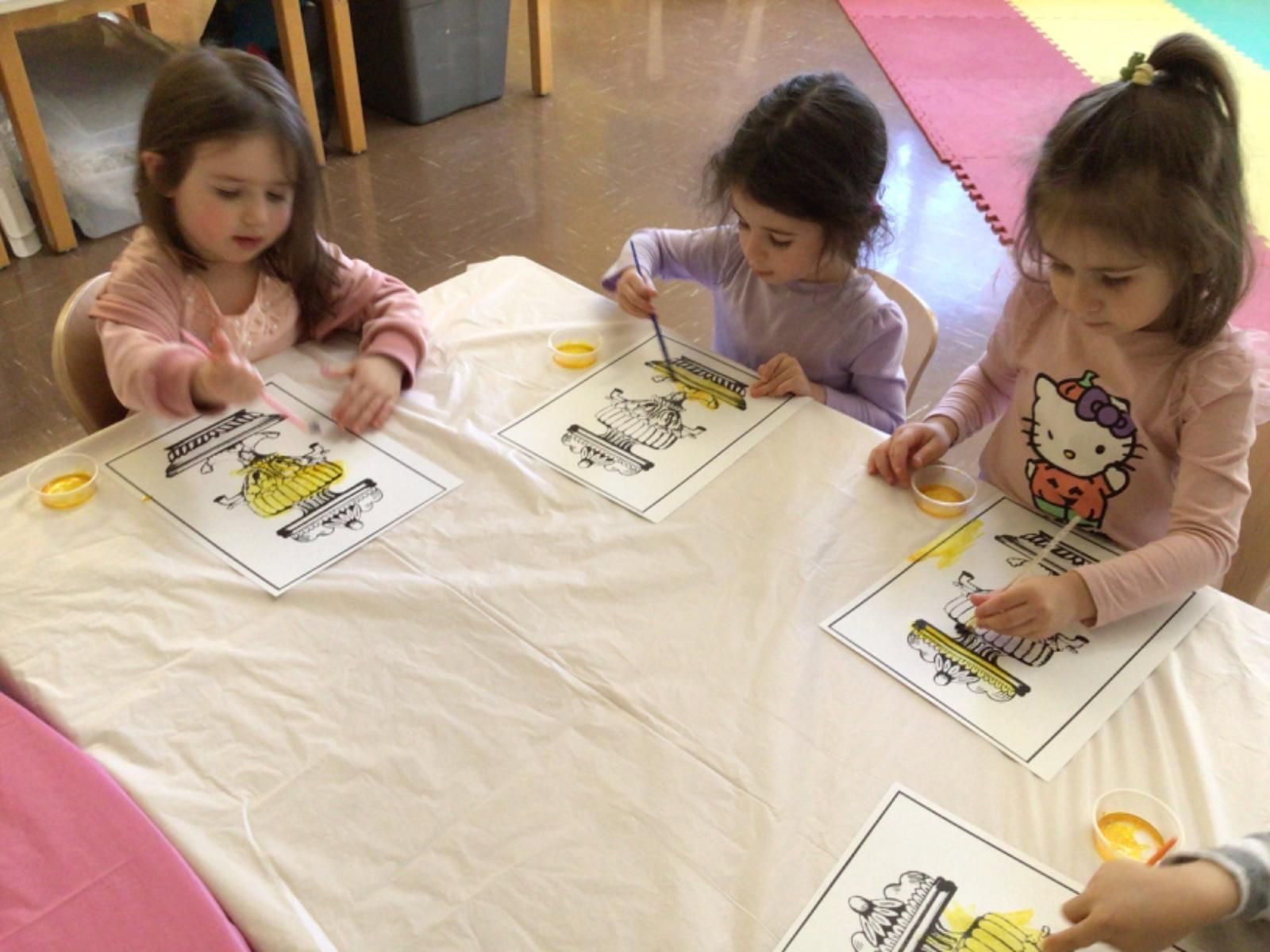 Three little girls are sitting at a table painting pictures