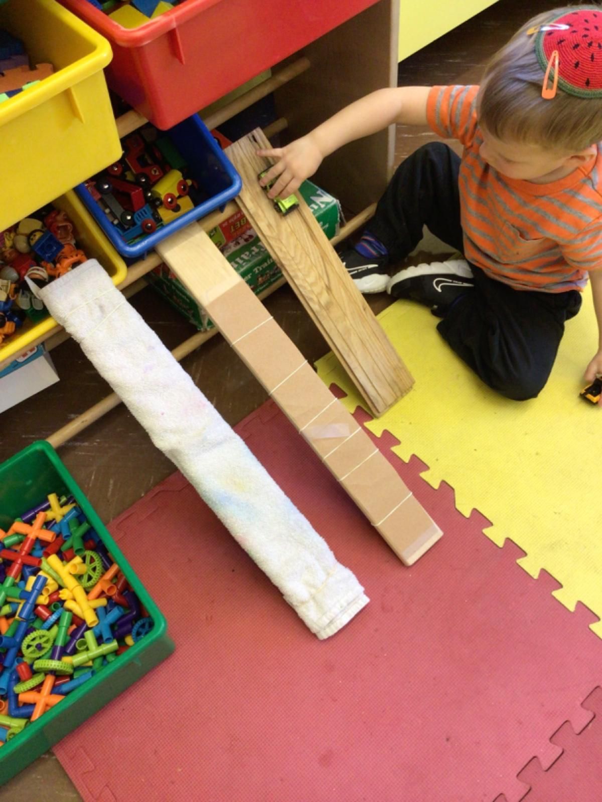 A child is playing with a toy car on a cardboard ramp