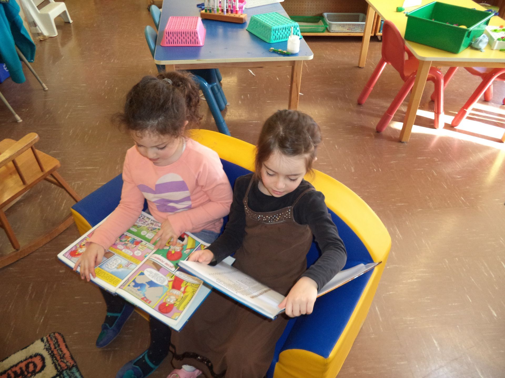 Two little girls are reading a book together in a classroom