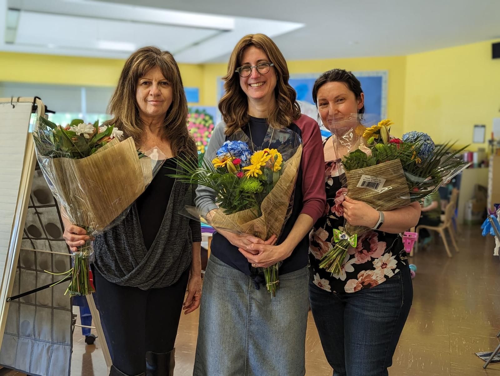Three women are standing next to each other holding bouquets of flowers.