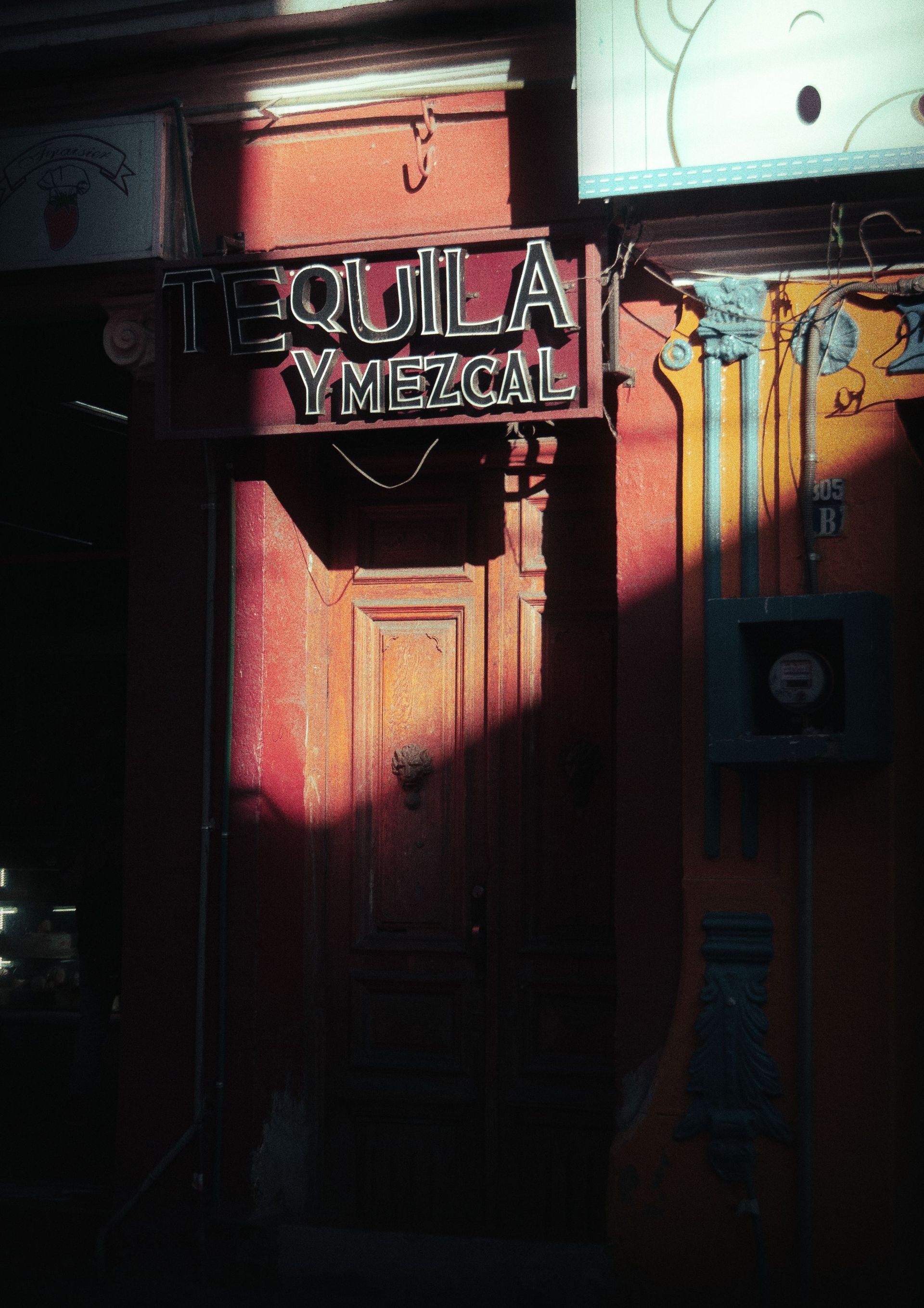 Entrada soleada con puerta de madera y un letrero que dice “SOTOLA MEZCAL” en una pared colorida.