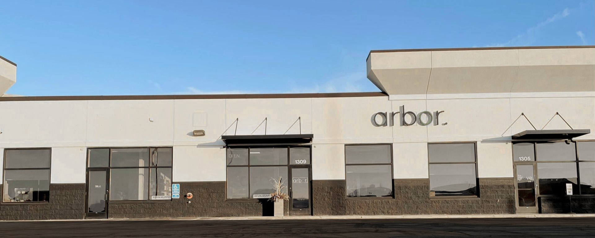 Exterior of the Arbor retail store with large windows and a sign against a blue sky.