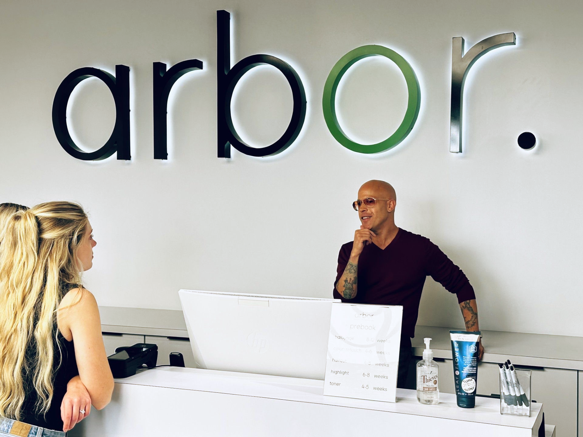 A customer and a staff member at the Arbor business's front desk. Signage above.