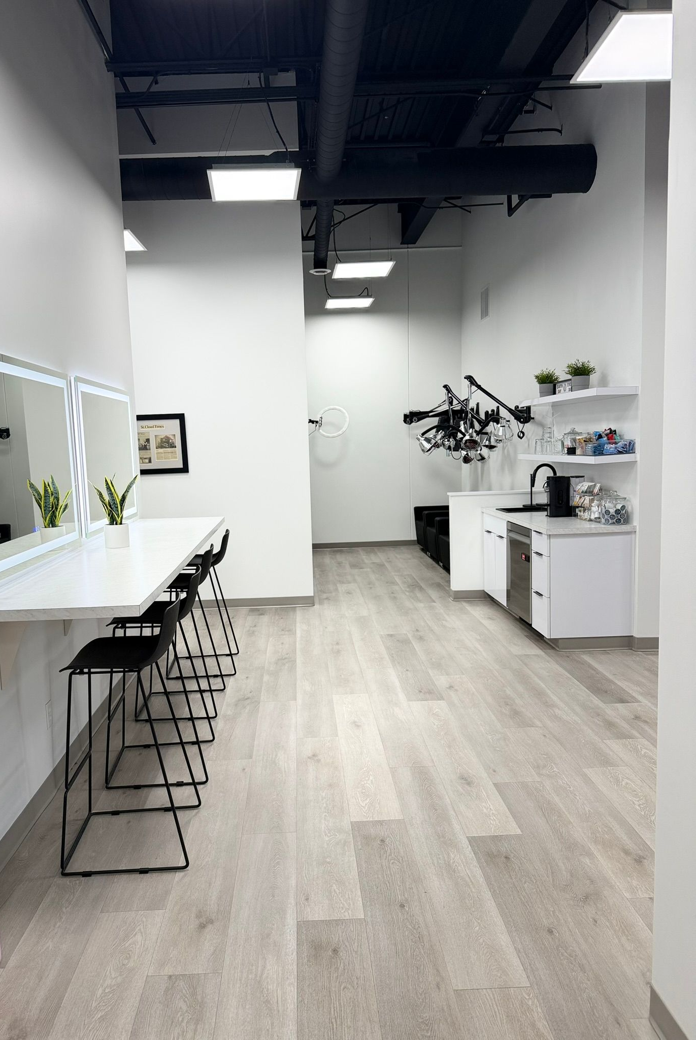 Makeup studio interior with lighted mirrors, stools, and a small kitchenette.
