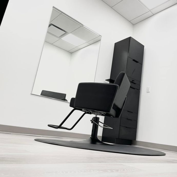Black salon chair, mirror, and storage unit in a bright, white room with a dark mat.
