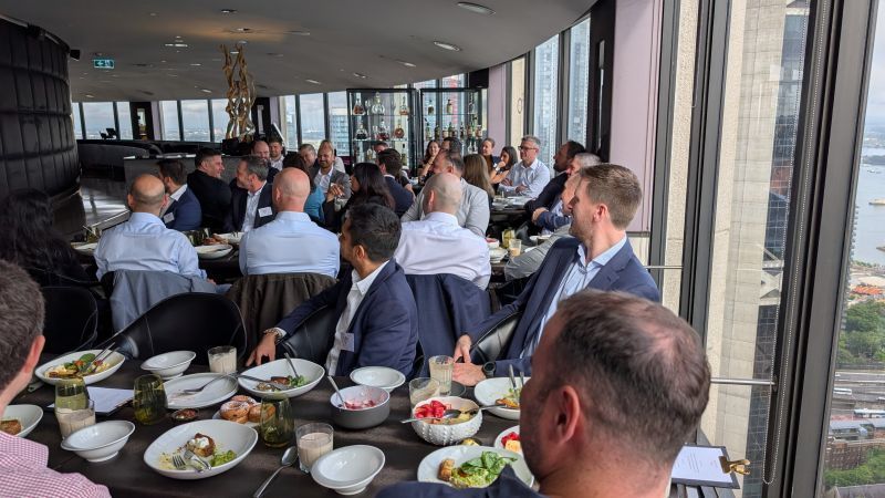 People seated at tables in a high-rise restaurant, eating, and talking, with city views.
