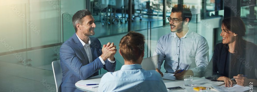 Four people in business attire are seated at a table, engaged in a discussion.