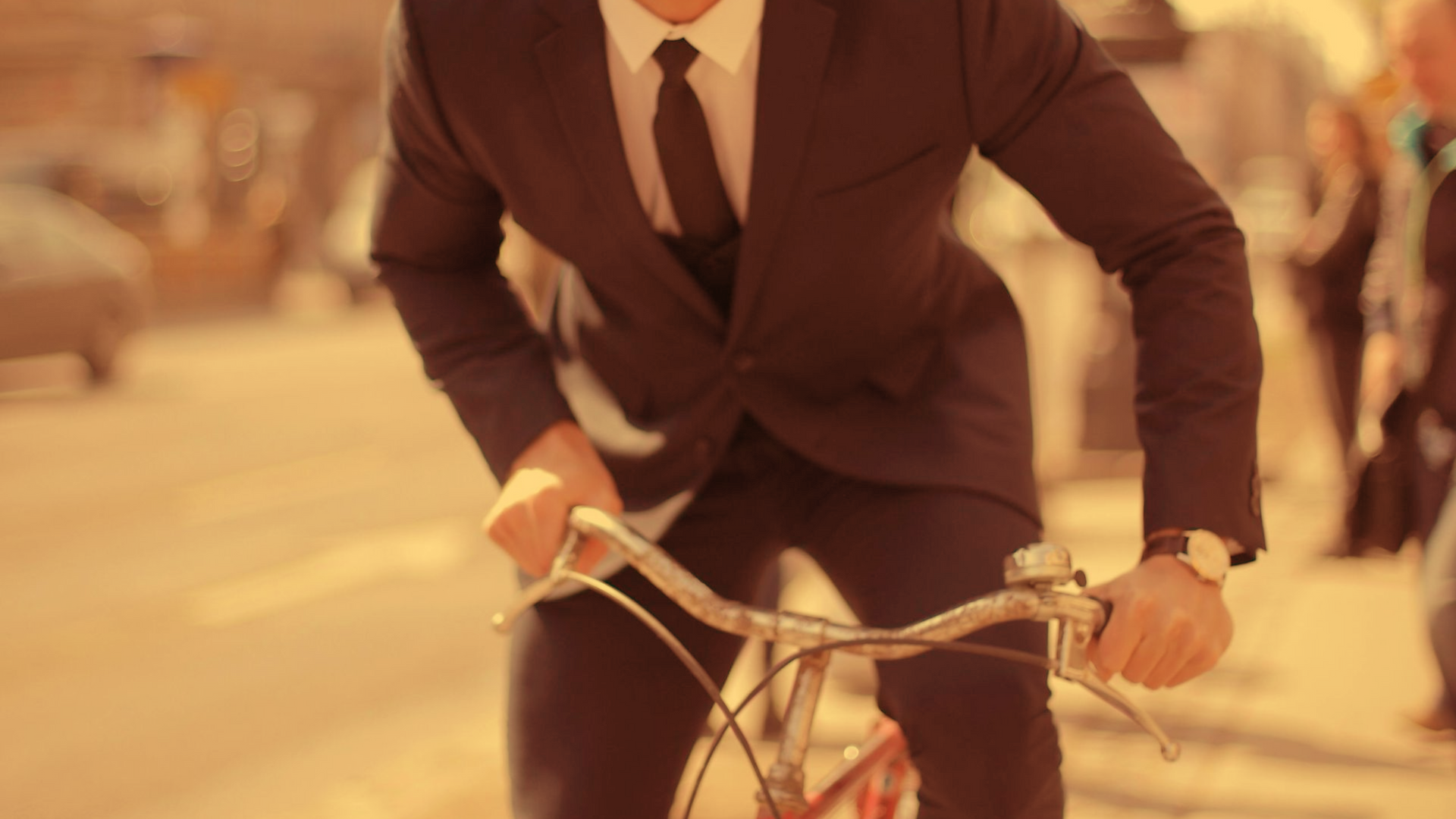 Man in suit riding a bicycle down a city street.