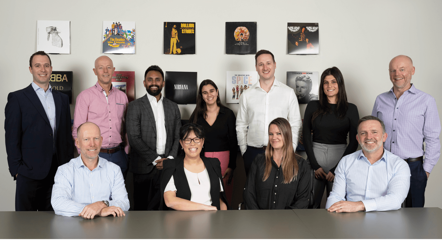 Group of people in business attire posing at a table, with records on the wall.
