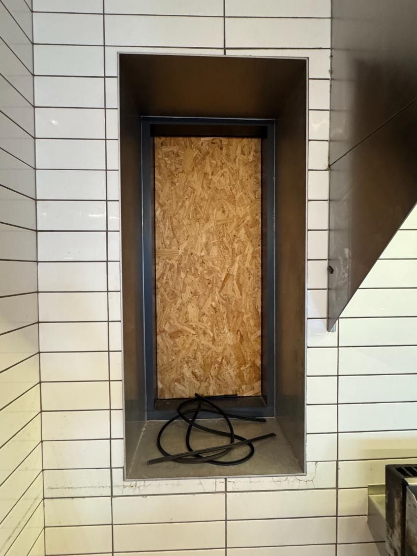 A white tiled wall with a window with a wooden board on it