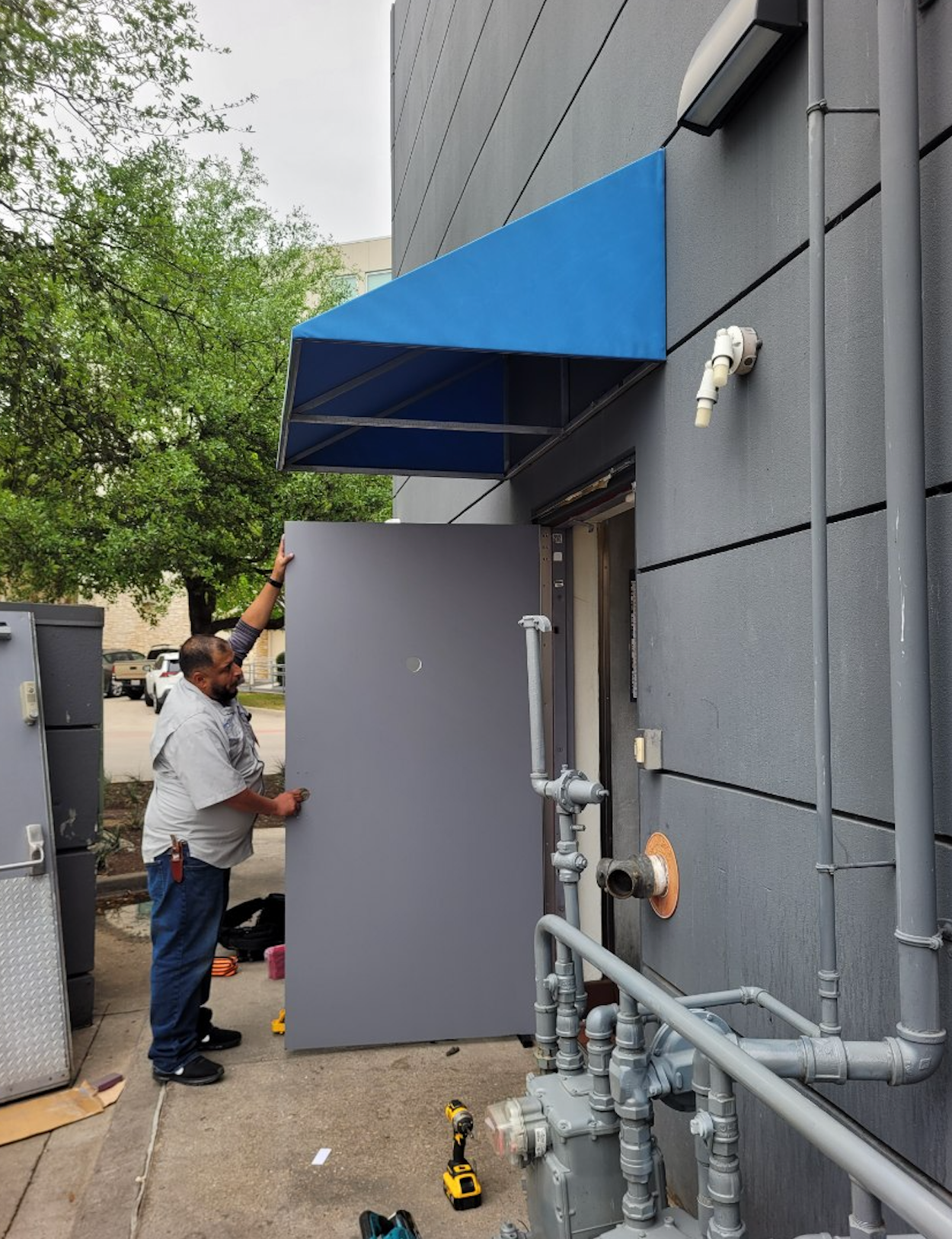 A man is installing a blue awning over a door