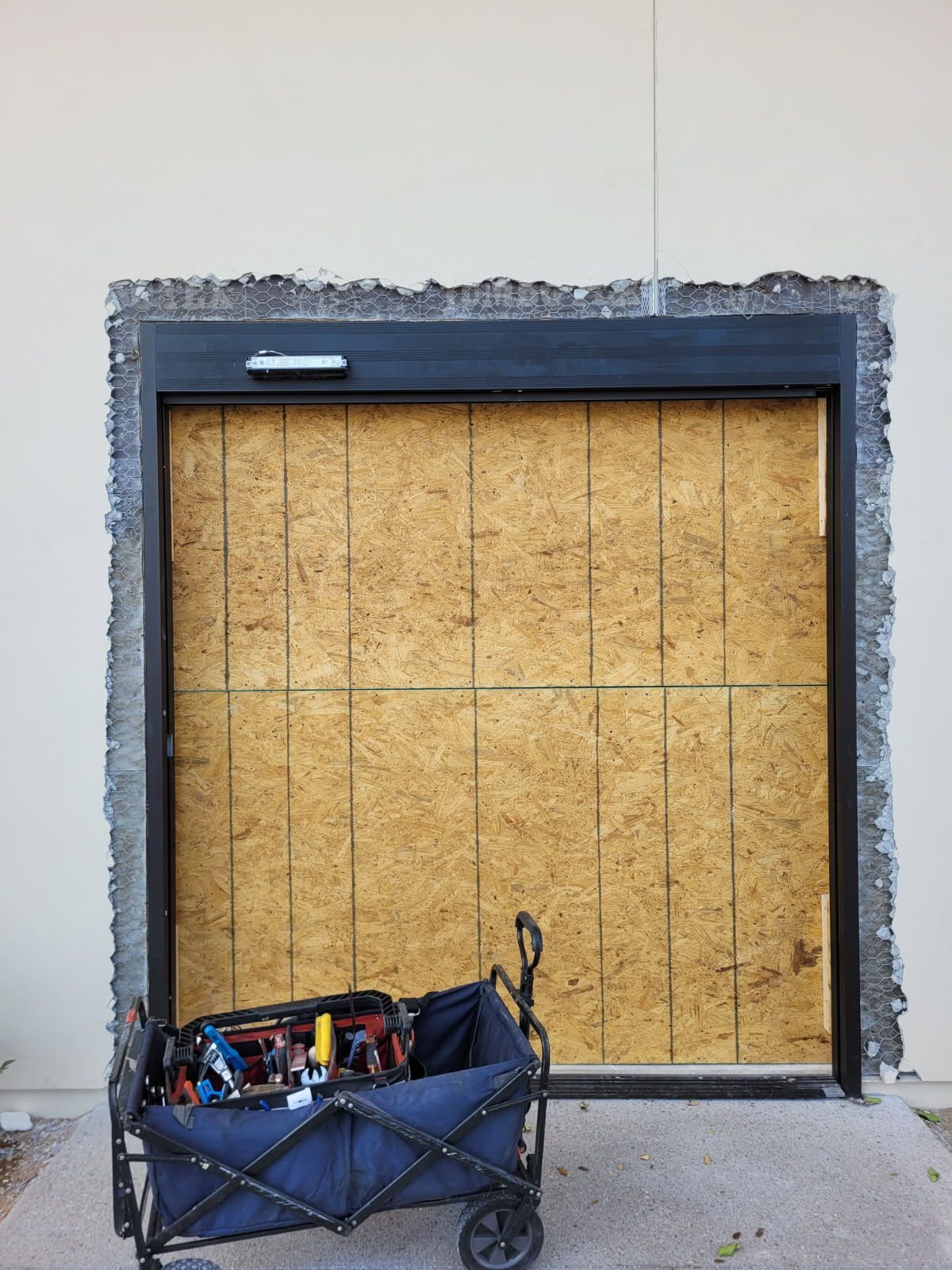 A blue wagon filled with tools is parked in front of a garage door.