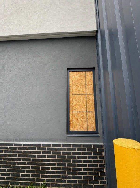 A building with a window boarded up and a yellow pole in front of it