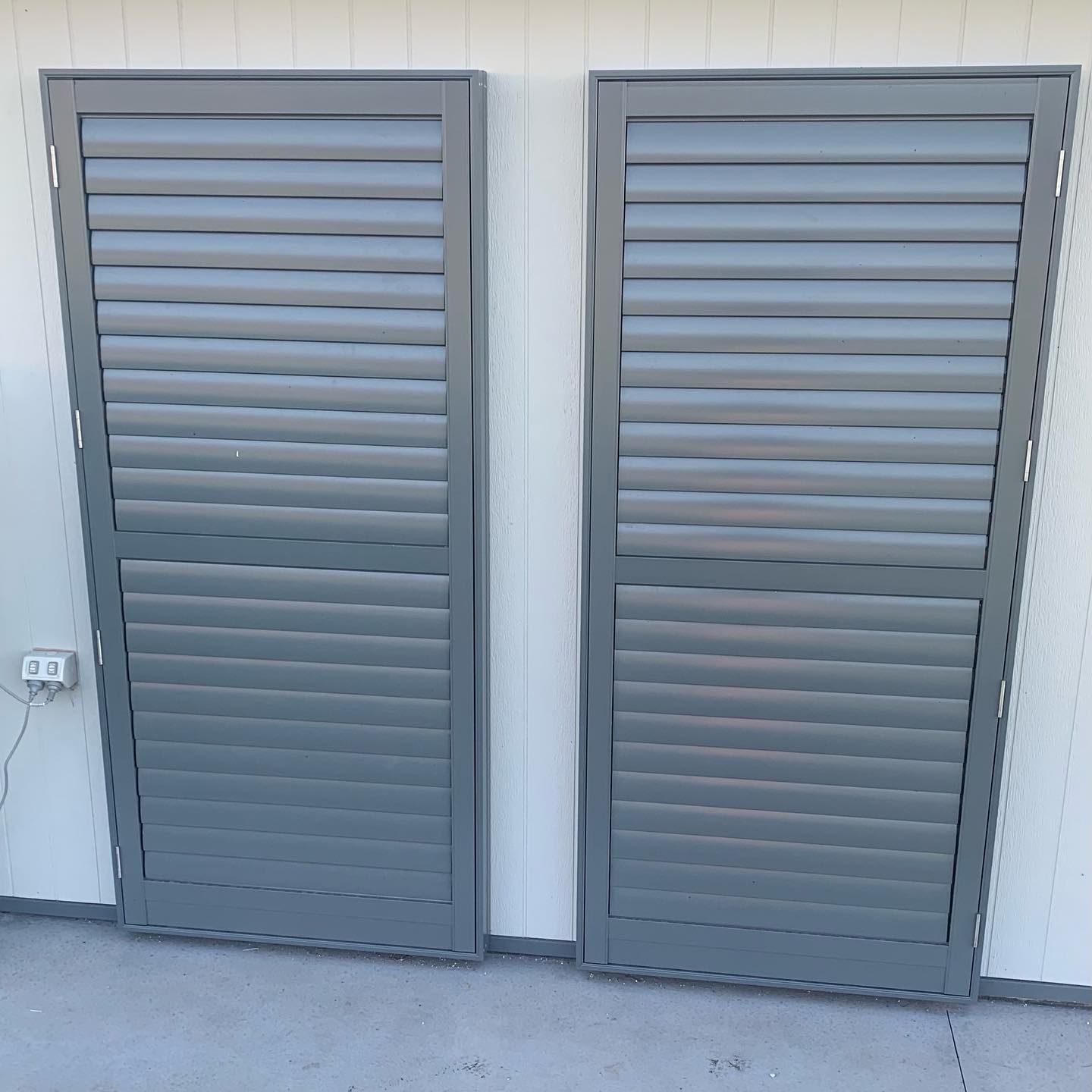 Two gray shutters are sitting next to each other on a white wall.
