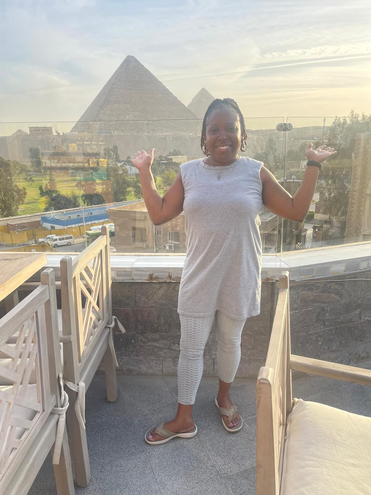 A woman is standing on a balcony with pyramids in the background.