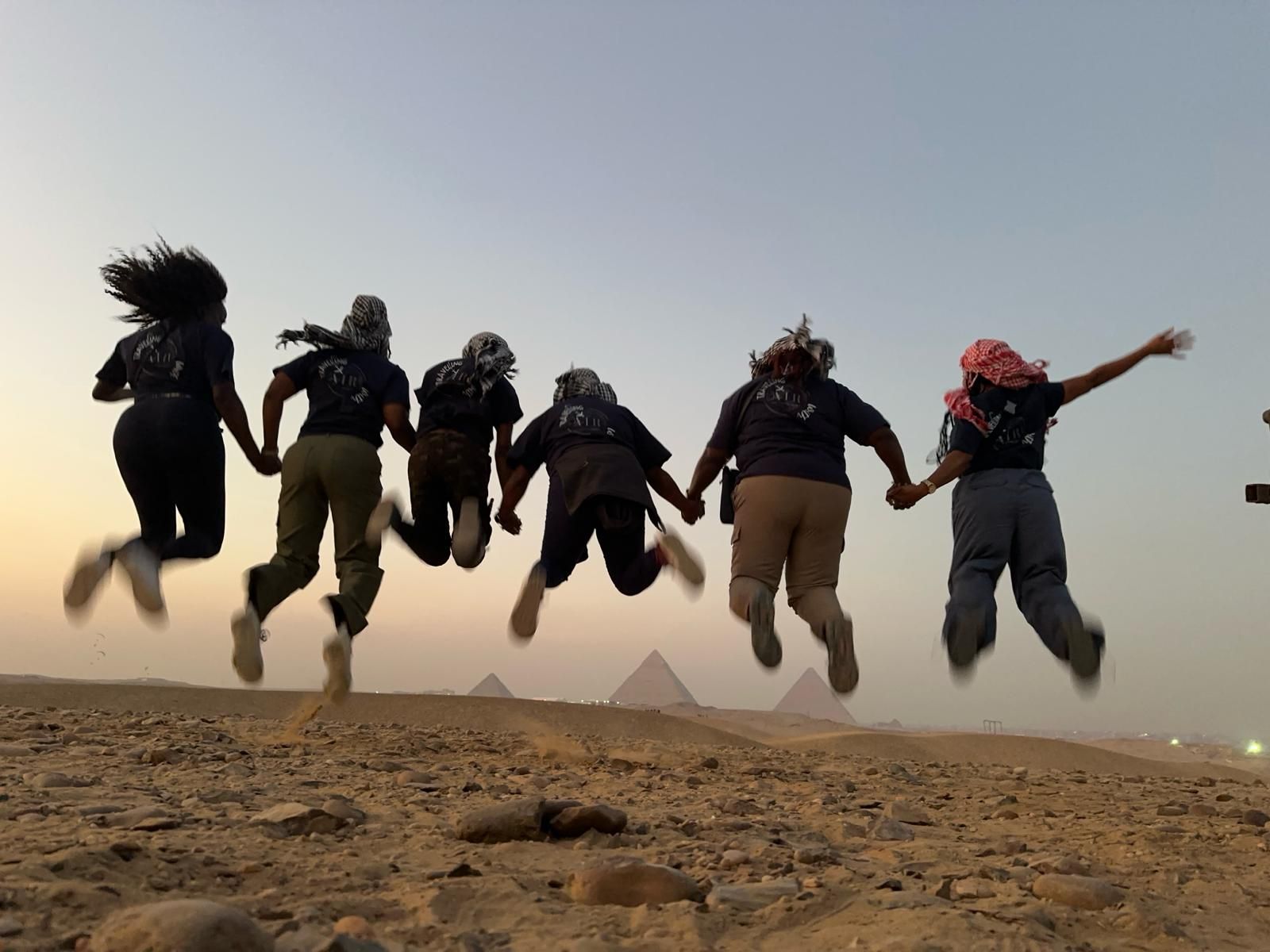 A group of people are jumping in the air in front of the pyramids
