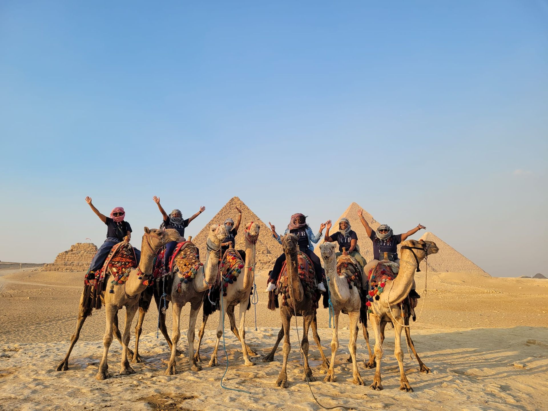 A group of people riding camels in front of the pyramids.