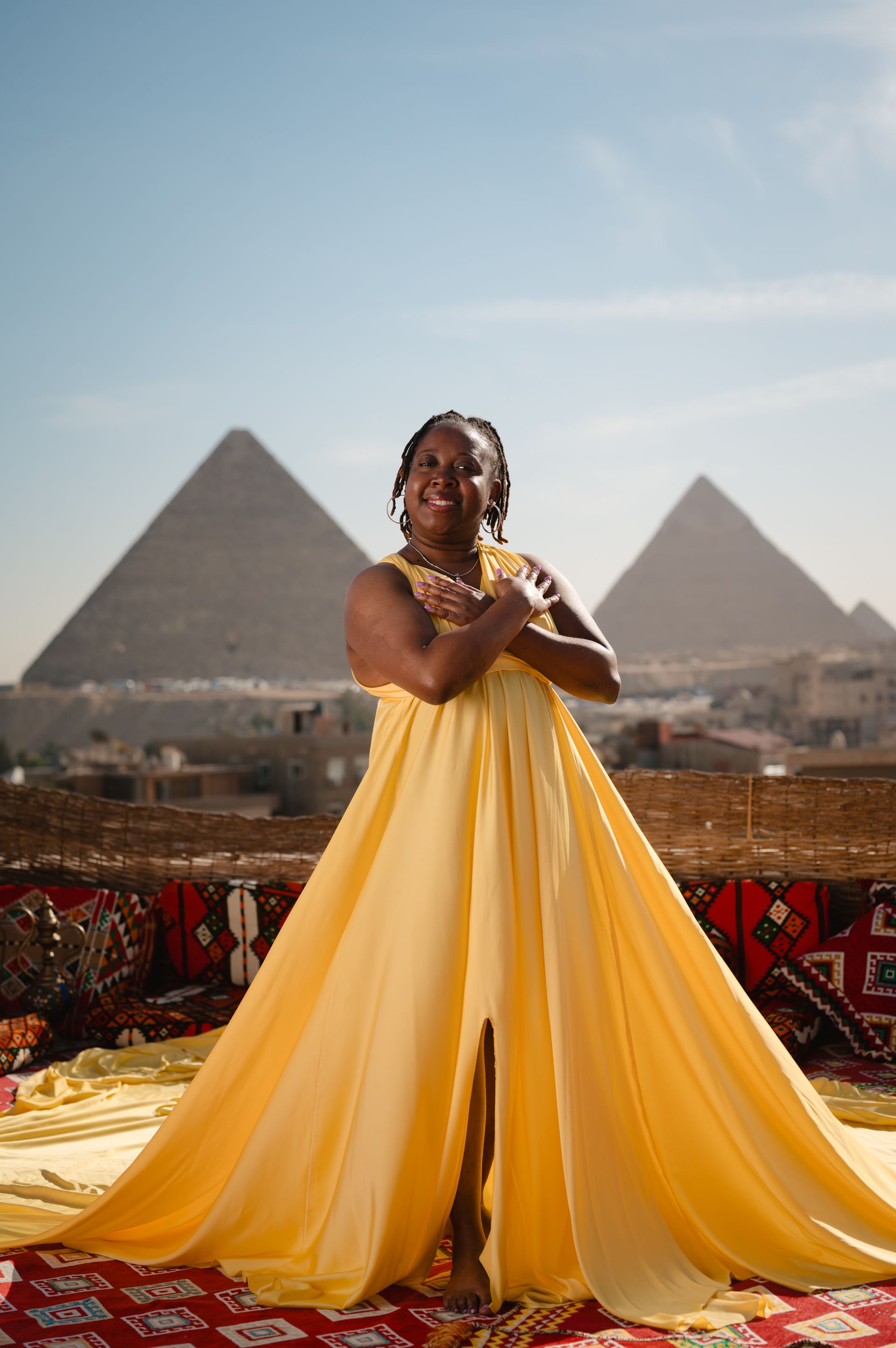 A woman in a long yellow dress is standing in front of two pyramids.