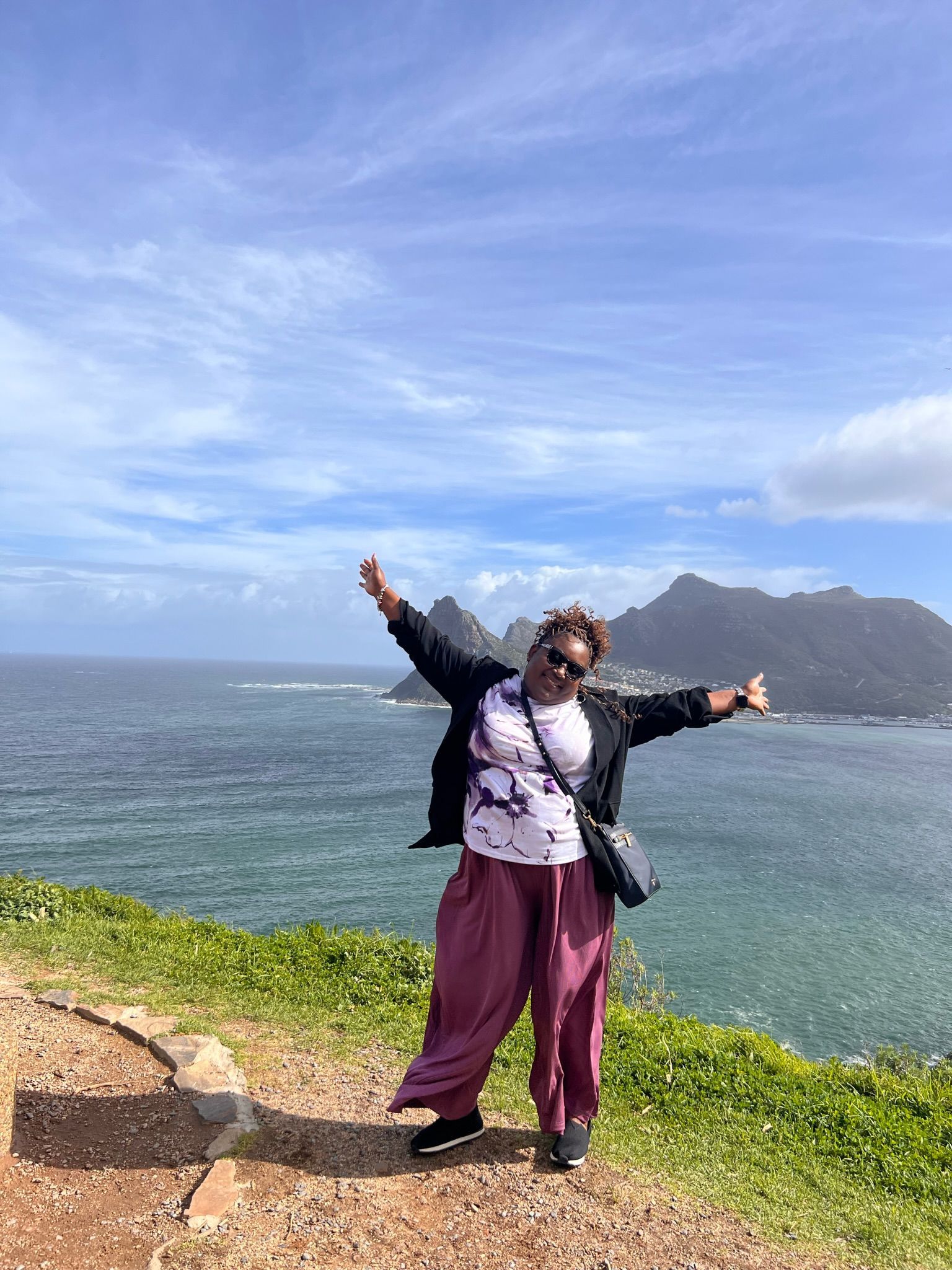 A woman is standing on a cliff overlooking the ocean with her arms outstretched.