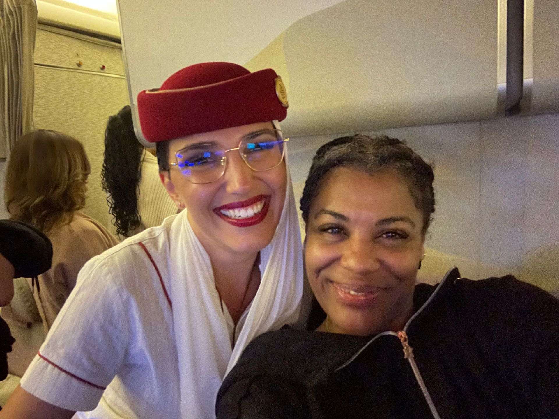 A flight attendant and a woman are posing for a picture on an airplane.