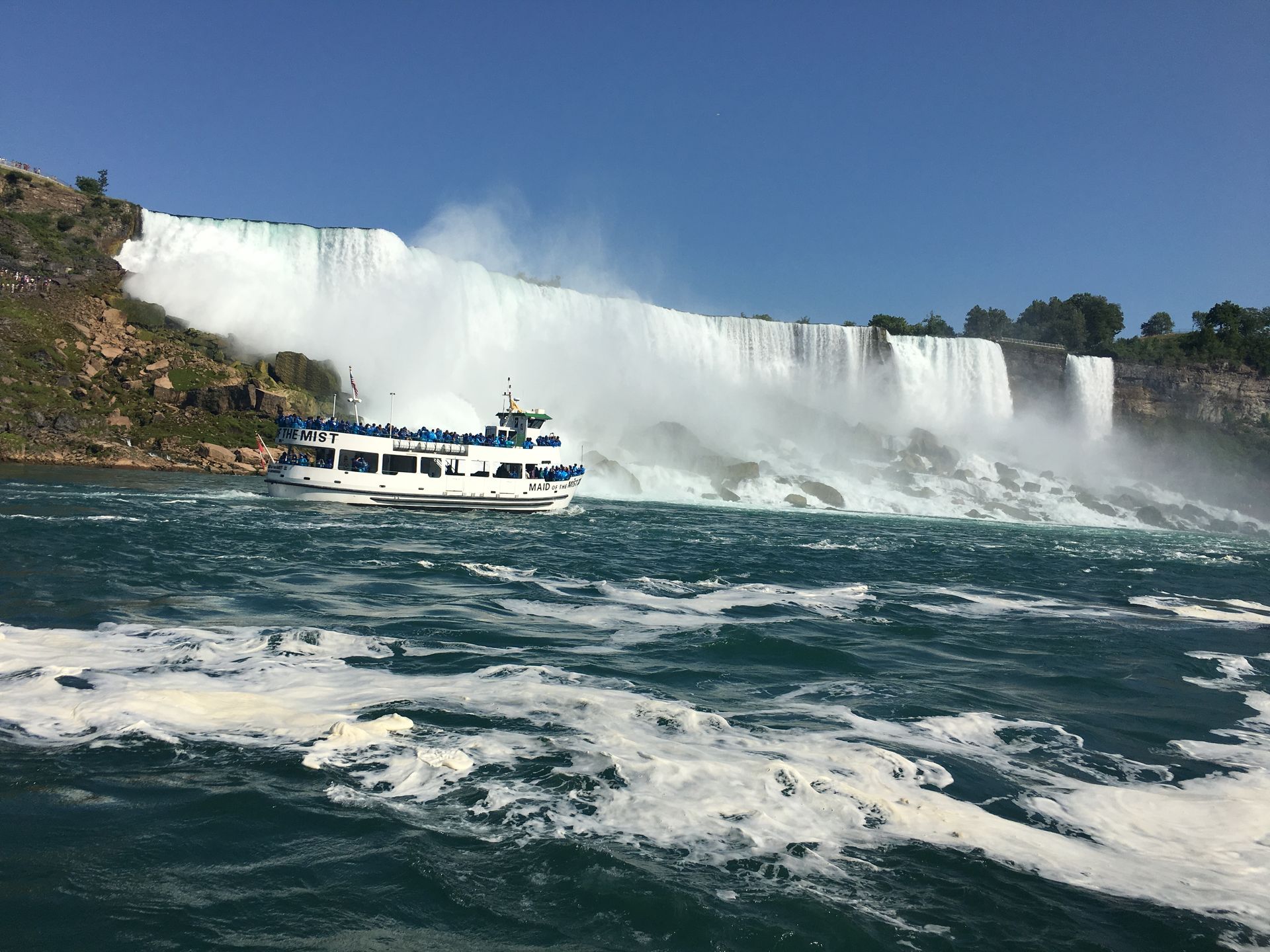 A boat is floating in front of a waterfall.