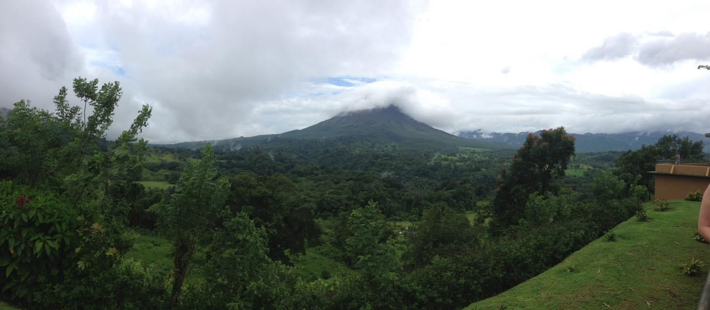A person is standing on a hill overlooking a mountain covered in clouds.
