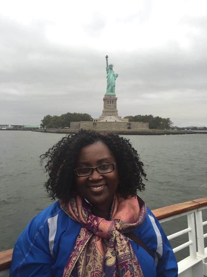 A woman is standing in front of the statue of liberty on a boat.