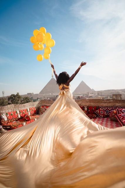 A woman in a long dress is holding balloons in front of the pyramids.