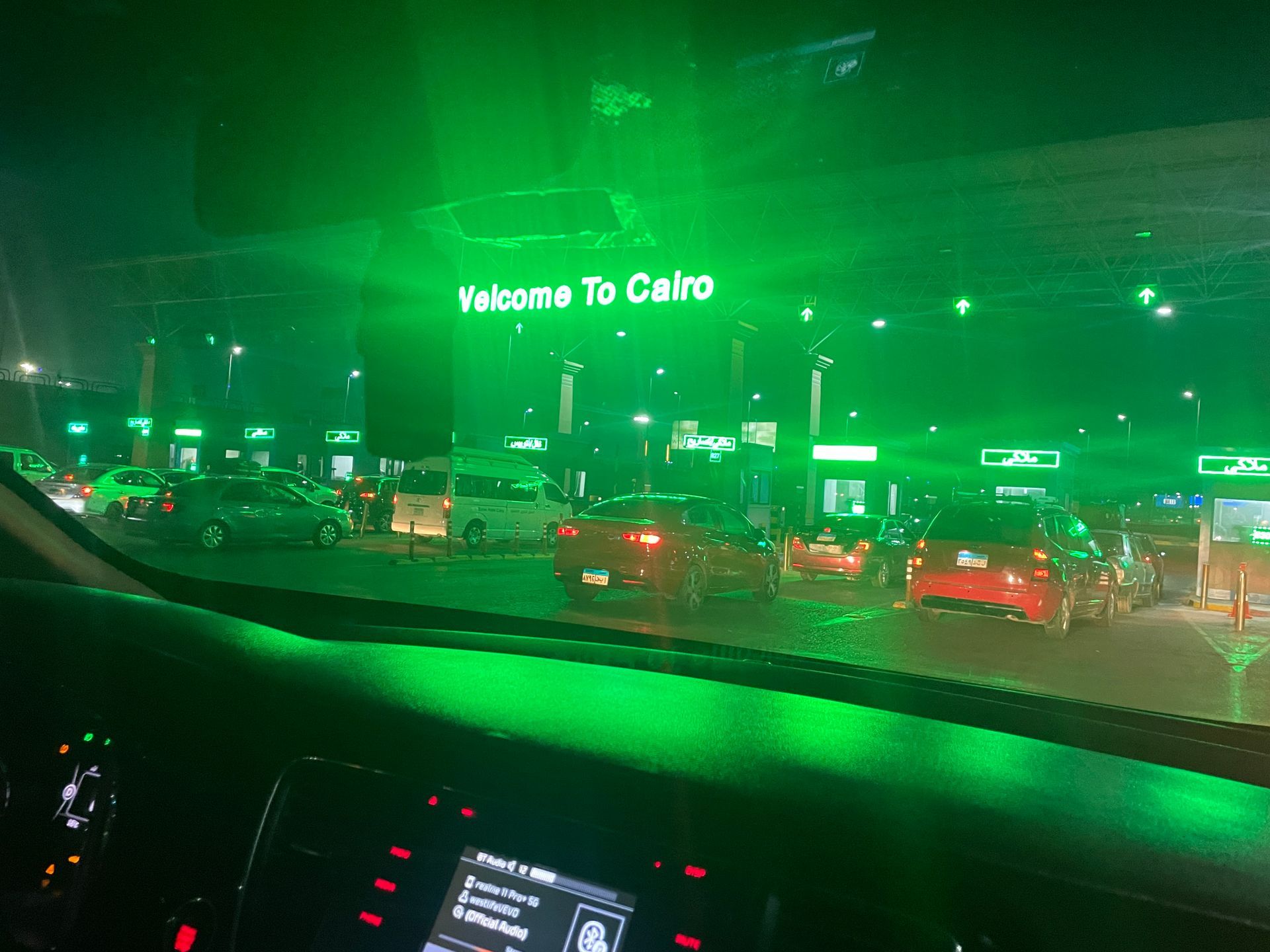 A car is driving down a street at night with a green sign that says welcome to cairo.