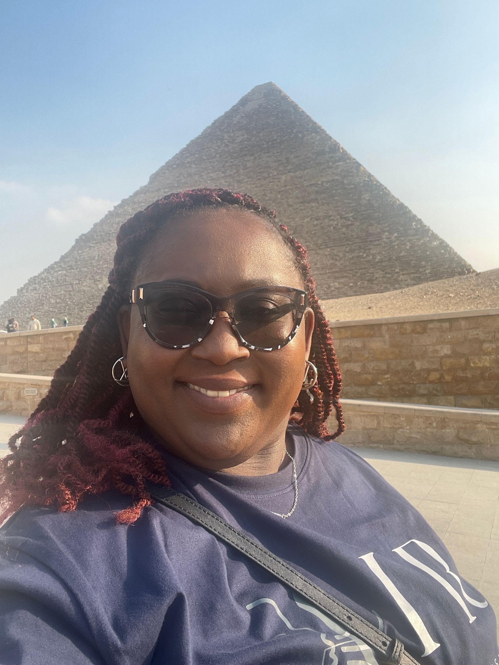 A woman wearing sunglasses is standing in front of a pyramid.