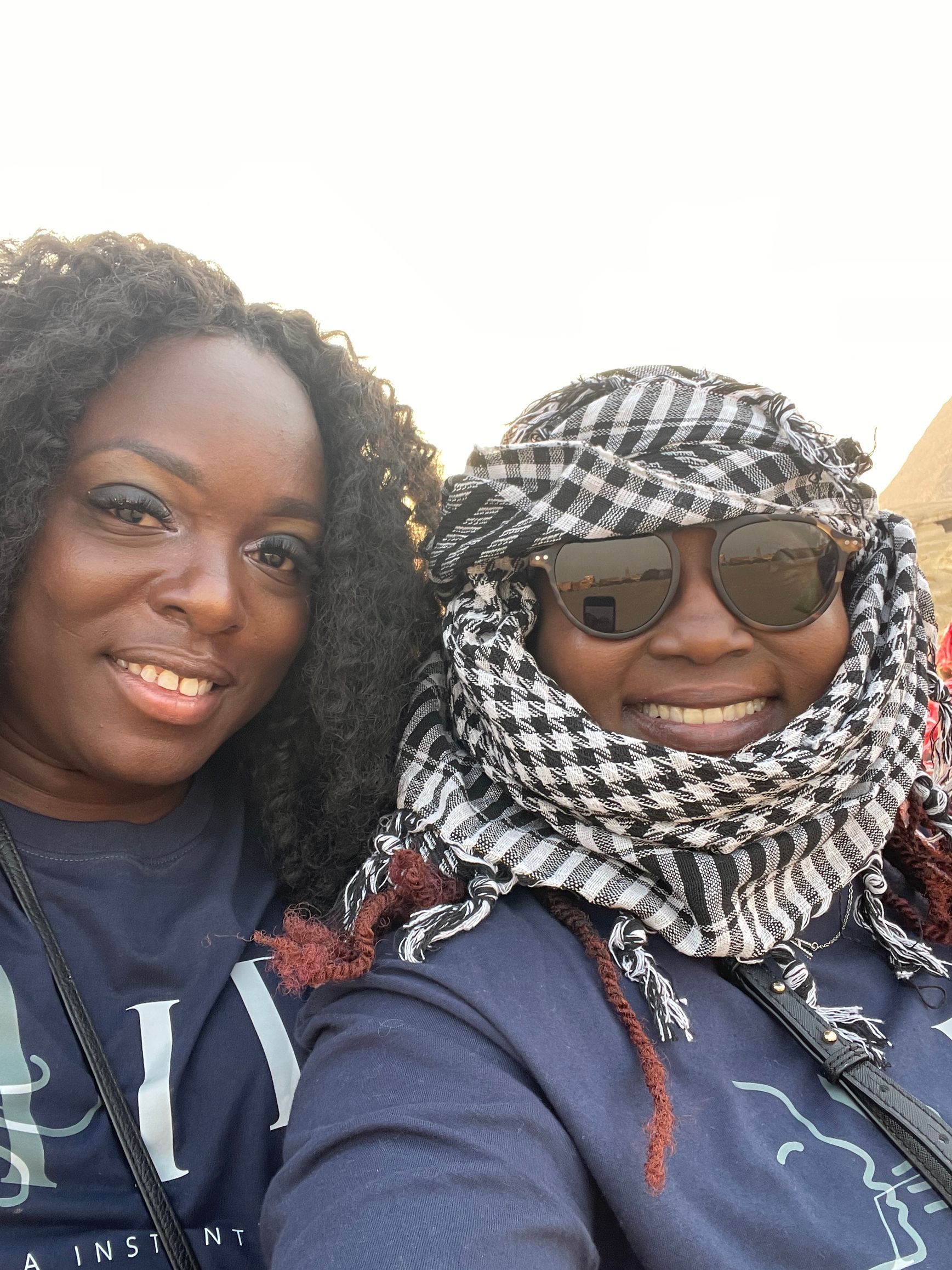 Two women wearing scarves and sunglasses are posing for a picture.