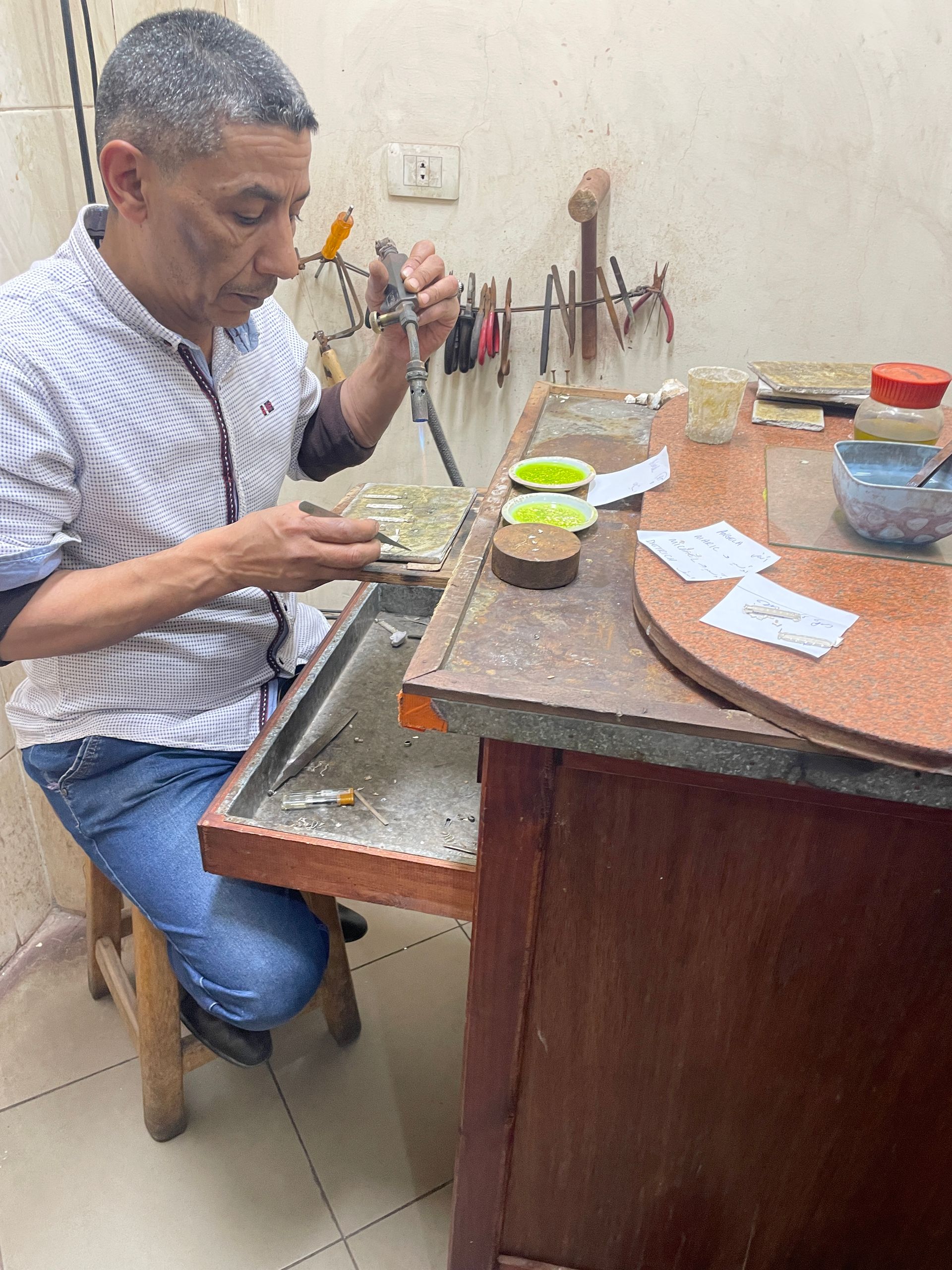 A man is kneeling down at a table working on a piece of metal.