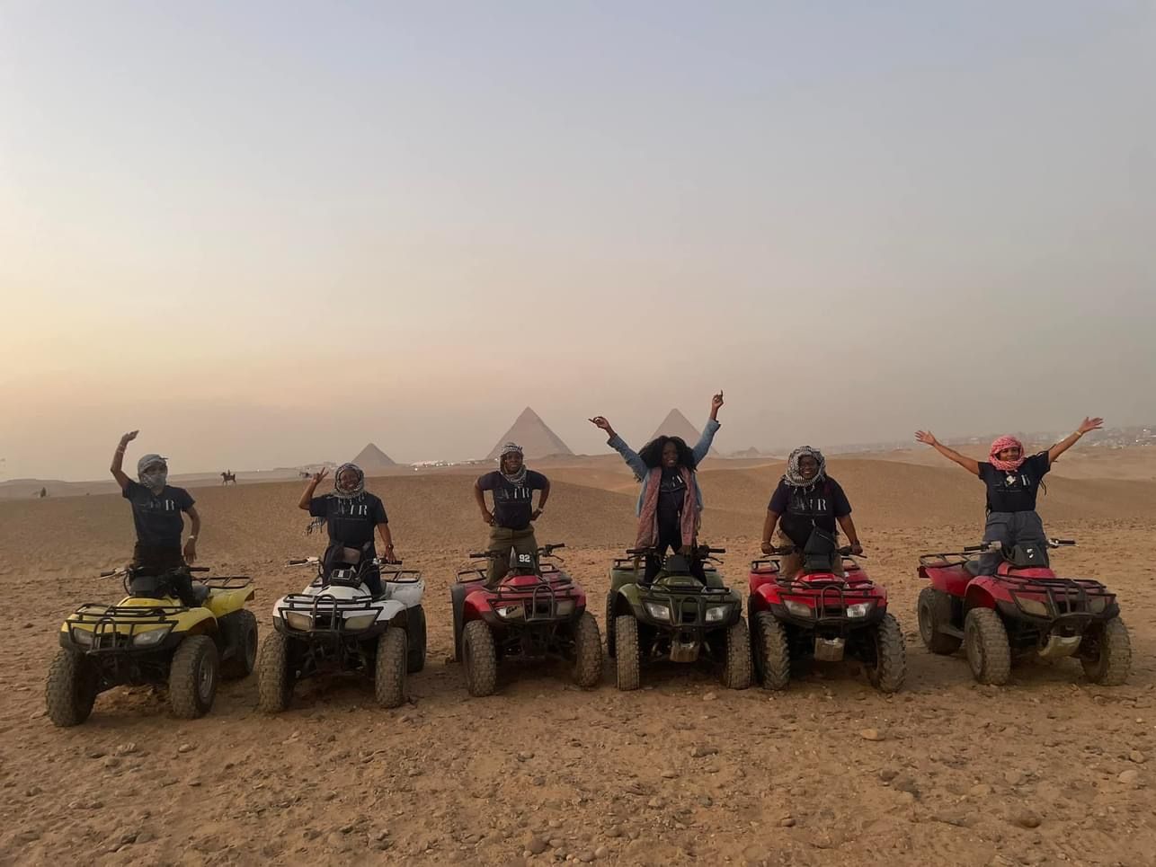 A group of people are riding atvs in the desert in front of the pyramids.