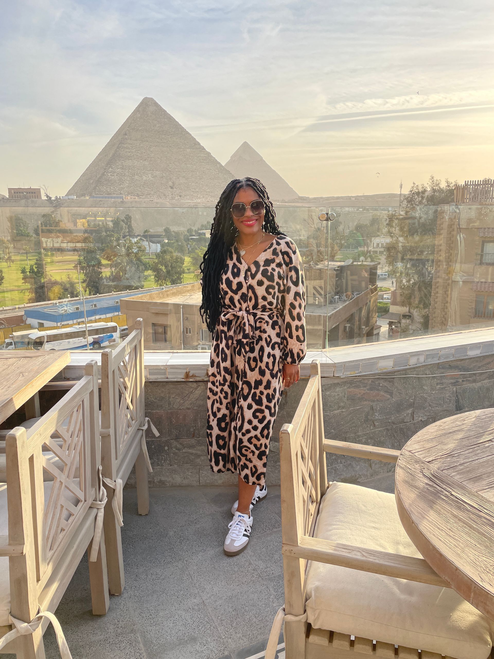 A woman in a leopard print dress is standing on a balcony overlooking the pyramids.