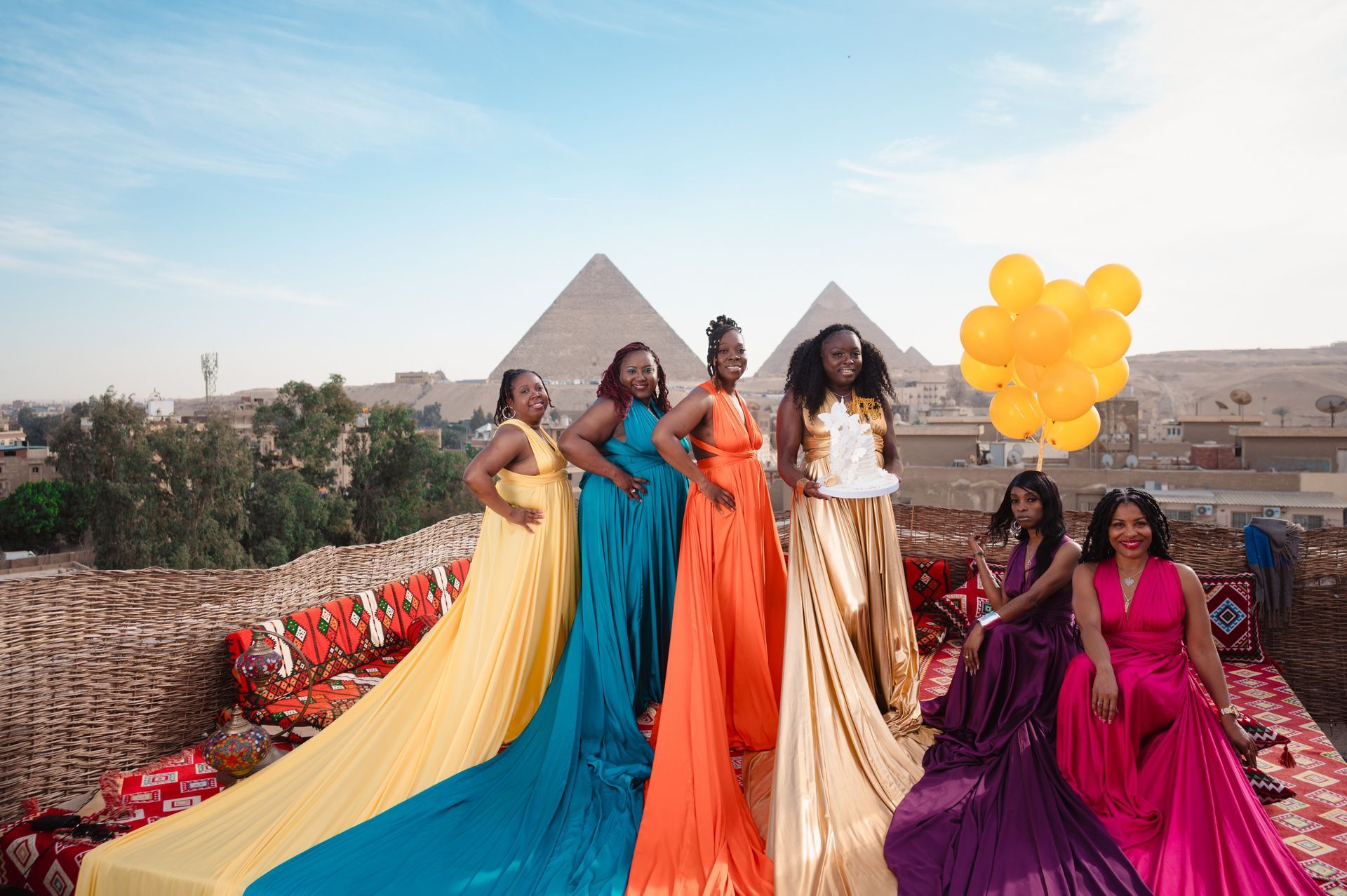 A group of women in long dresses are standing next to each other in front of the pyramids.