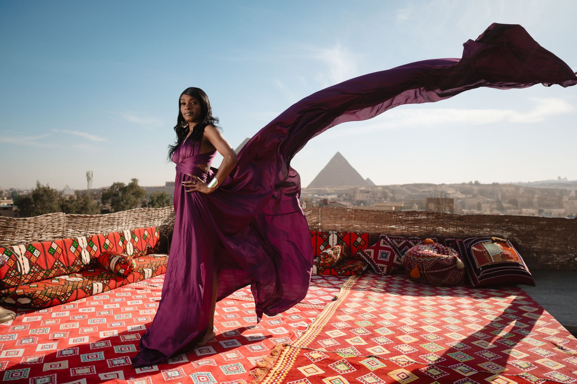 A woman in a purple dress is standing on a red rug with a pyramid in the background.