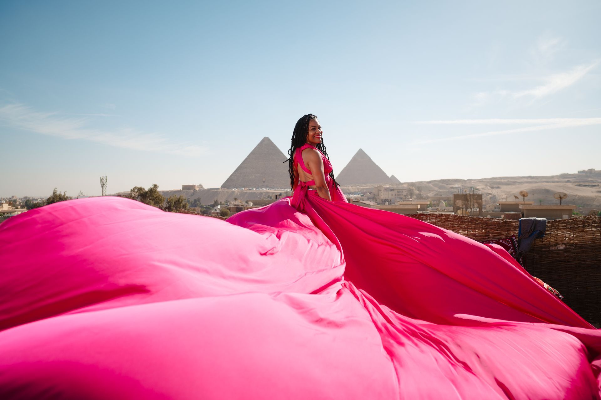 A woman in a long pink dress is standing in front of the pyramids.