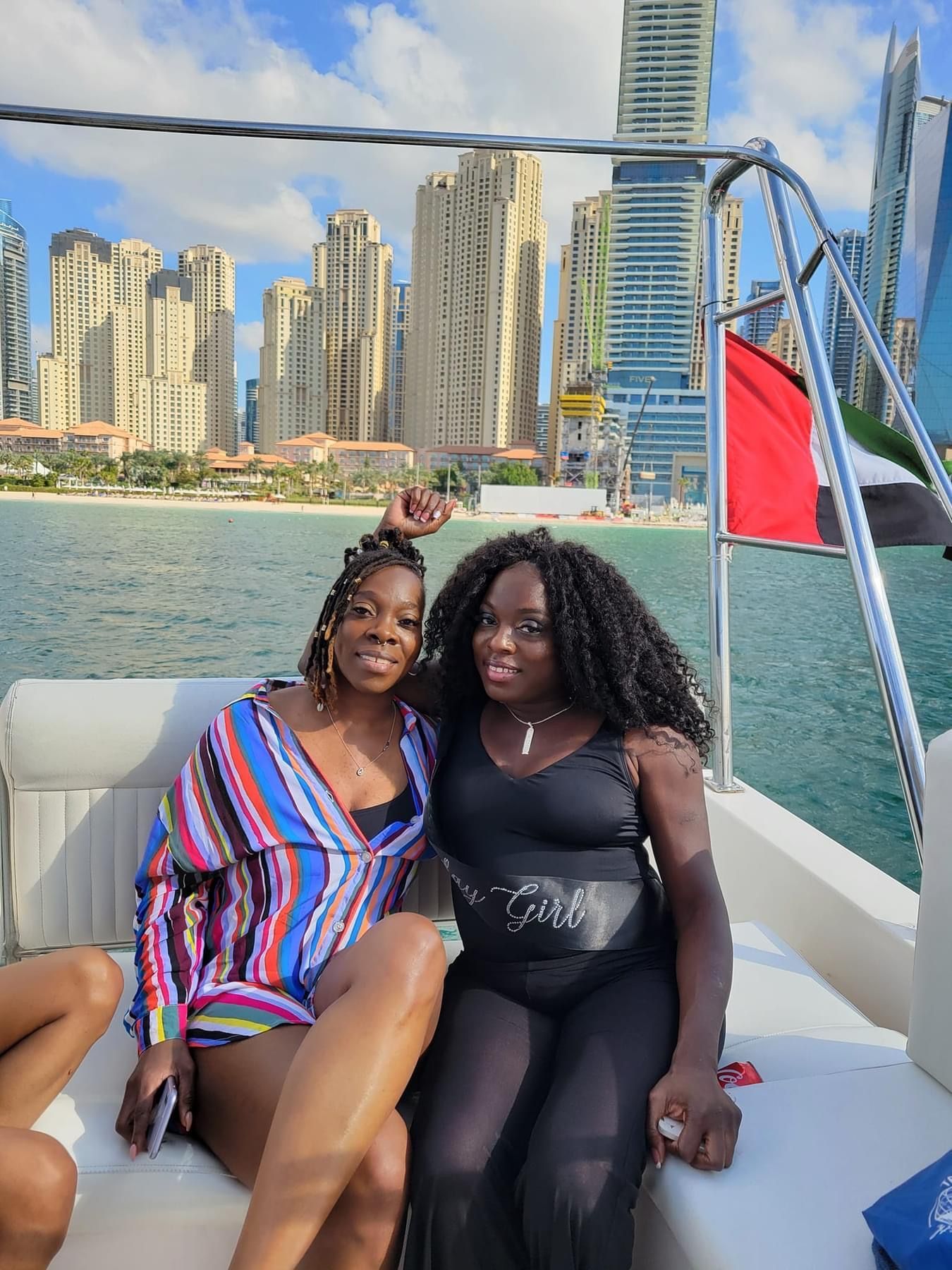 Two women are sitting on a boat with a city in the background.