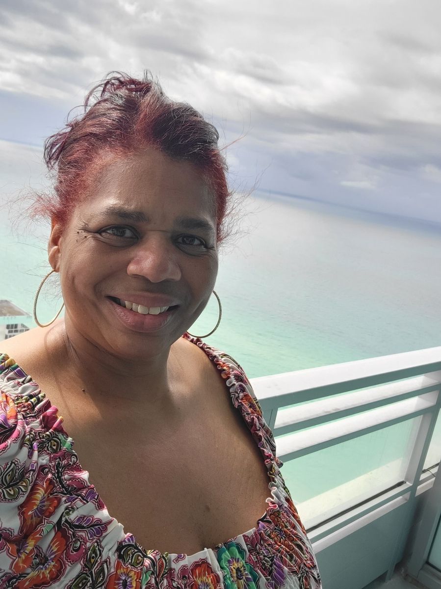 A woman is smiling while standing on a balcony overlooking the ocean.