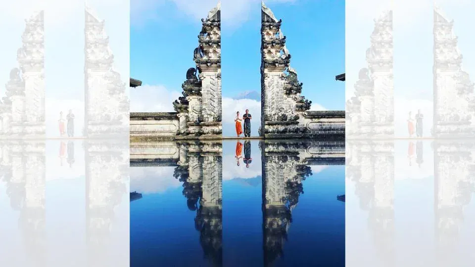 A couple standing in front of a temple with their reflection in the water.