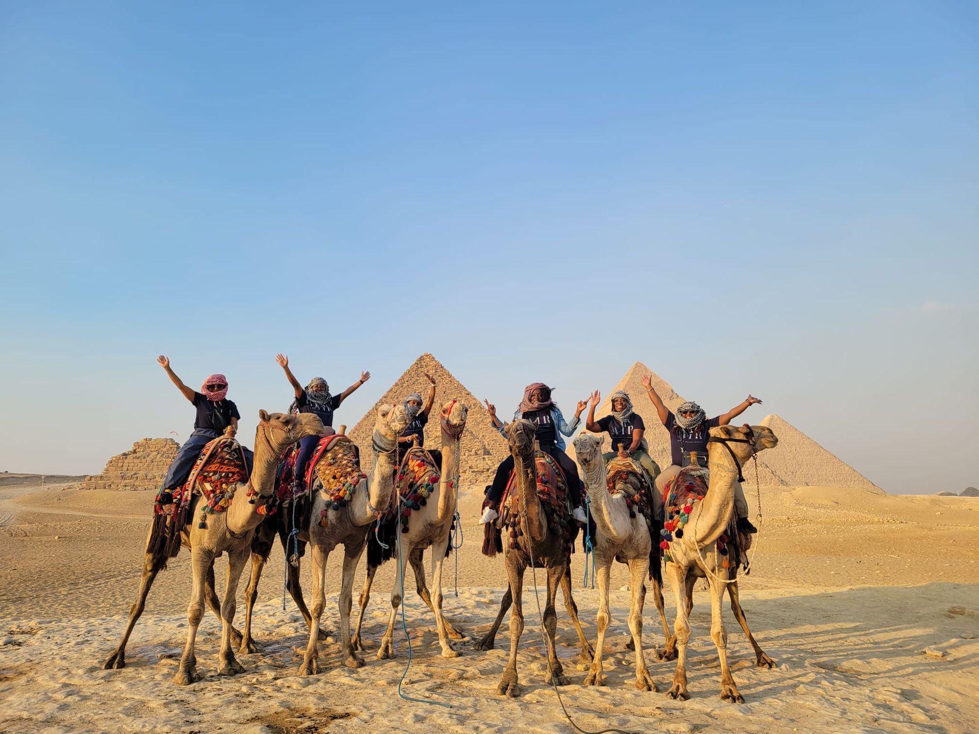 A group of people riding camels in front of the pyramids.