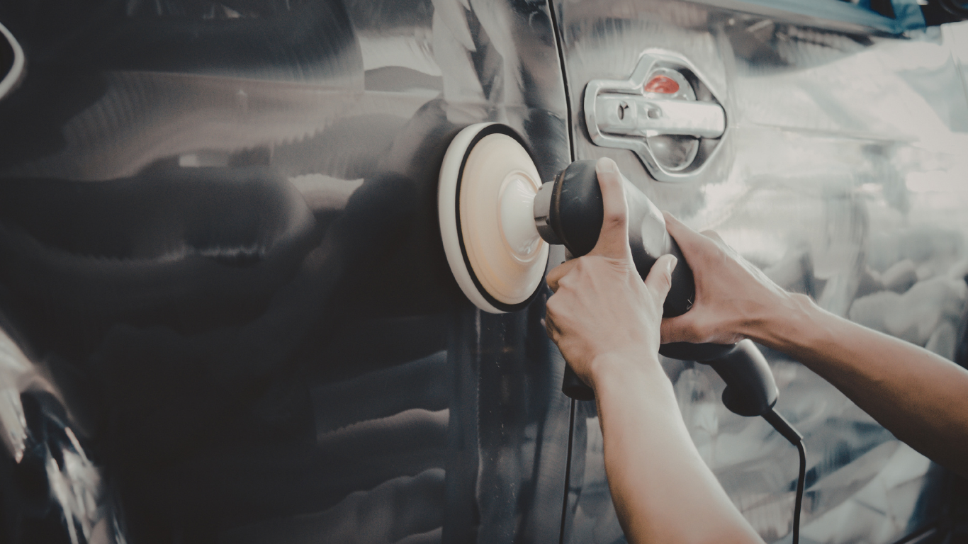 Person polishing a dark car door with a power buffer.